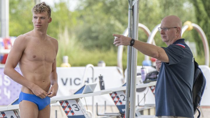 Léon Marchand reçoit les dernières consignes de son coach américain, Bob Bowman, avant de plonger pour une séance d'entraînement dans le bassin du stade aquatique de Vichy, à l'occasion du stage de préparation des Bleus pour les Jeux olympiques de Paris, le 24 juillet 2024. (KEMPINAIRE STEPHANE / AFP)