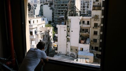 Un homme regarde à travers une fenêtre sans vitre les dégats de l'explosion du 4 août 2020, qui a fait 214 morts et plus de 6 500 blessés, le 9 juillet 2021. (ALINE LAFOY / HANS LUCAS / AFP)