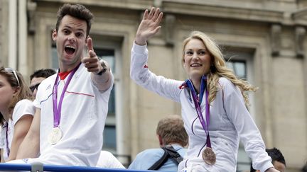 Le nageur Gregory Mallet et la championne de taekwondo Marl&egrave;ne Harnois saluent la foule depuis le toit de leur bus. (KENZO TRIBOUILLARD / AFP)