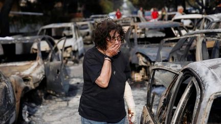 Une femme tente de retrouver son chien parmi les voitures calcinées du village de Mati, mardi 24 juillet 2018. Cette petite station balnéaire est très prisée des touristes, en particulier des retaités et des enfants en colonies de vacance.&nbsp; (COSTAS BALTAS / REUTERS)