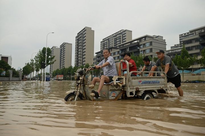 Des habitants de Zhengzhou, dans la province du Henan (Chine), traversent une rue inondée, le 22 juillet 2021. (NOEL CELIS / AFP)