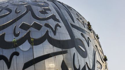 Des travailleurs nettoyant la calligraphie arabe à l'extéireur du Musée du Futur à Dubaï.&nbsp; (KARIM SAHIB / AFP)