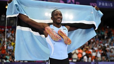 Letsile Tebogo célèbre sont titre olympique avec le drapeau du Botswana après avoir remporté la finale du 200 m masculin de l'épreuve d'athlétisme aux Jeux Olympiques de Paris, le 8 août 2024, au Stade de France à Saint-Denis. (BEN STANSALL / AFP)