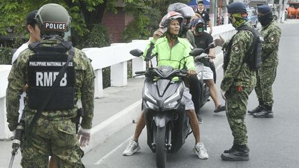 Des officiers de police armés arrêtent un motard à un checkpoint à Manille, le 15 mars 2020. (MAXPPP)