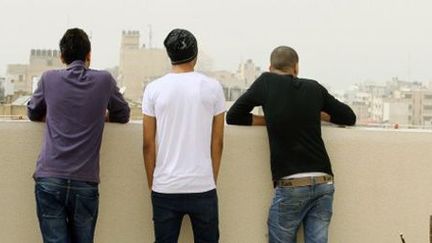 Ces trois jeunes hommes, qui regardent la ville de Gaza du haut d'une terrasse, se sont fait couper les cheveux de force par les services de sécurité du territoire palestinien. (AFP - MOHAMMED ABED)