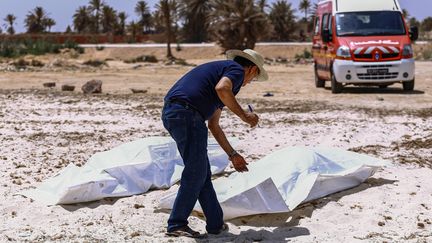 Sur une plage d'Aghir, dans l'île de Djerba, au sud de la Tunisie, un&nbsp;membre du Croissant-Rouge tunisien vérifie les corps de migrants dont le bateau a chaviré au large des côtes tunisiennes alors qu'ils traversaient la Méditerranée entre la Libye et l'Italie (6 juillet 2019). (ANIS MILI / AFP)