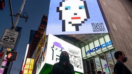 Passante devant le NFT "CryptoPunk" projeté sur un&nbsp;panneau d'affiche numérique à Time Square, à New York, en mai 2021.&nbsp; (ALEXI ROSENFELD / GETTY IMAGES NORTH AMERICA)