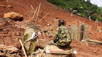 Un soldat est assis devant une colline éboulée à Freetown (Sierra Leone), après les inondations qui ont ravagé la ville, le 18 août 2017.&nbsp; (SEYLLOU / AFP)