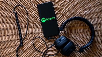 Masque connecté à un téléphone mobile dont l'écran affiche le logo de Spotify, leader mondial des plateformes audio. (NIKOS PEKIARIDIS / NURPHOTO / AFP)