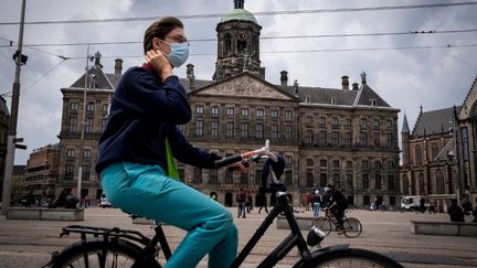 Un cycliste roule masqué devant la place du Dam à Amsterdam (Pays-Bas), le 20 mai 2021. (MARTIN BERTRAND / HANS LUCAS)
