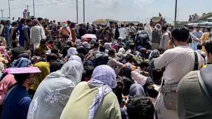 Des Afghans le long d'une route en attendant de monter à bord d'un avion militaire américain pour quitter le pays,&nbsp;à&nbsp;l'aéroport militaire de Kaboul, le 20 août 2021.&nbsp; (WAKIL KOHSAR / AFP)