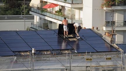 Des ouvriers posent des panneaux solaires sur le toit d'un immeuble ancien. Illustration (BRUNO LEVESQUE / MAXPPP)