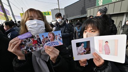 Des fans du groupe BTS montre des photos de Jin, l'aîné du groupe de K-pop contraint d'entamer son service militaire mardi 13 décembre 2022, à Yeoncheon (Corée du Sud). (JUNG YEON-JE / AFP)