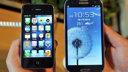 Un employ&eacute; montre un&nbsp;iPhone 4S d'Apple (G) et un Samsung Galaxy S3 (D), dans une boutique de t&eacute;l&eacute;phones portables de S&eacute;oul (Cor&eacute;e du Sud), le 27 ao&ucirc;t 2012. (JUNG YEON-JE / AFP)