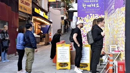 Des passants lisent des messages en mémoire des victimes d'une bousculade meurtrière un an plus tôt, le 23 octobre 2023 à Séoul (Corée du Sud). (KAZUKI KOIKE / YOMIURI / AFP)