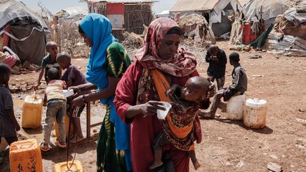 Une mère de famille somalienne donne de l'eau à son enfant dans un camp de déplacés à Baidoa (Somalie), le 14 février 2022.&nbsp; (YASUYOSHI CHIBA / AFP)