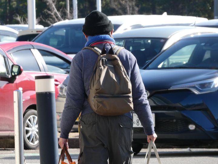 Norimitsu Funamoto, réfugié de la ville de Suzu,  photographié de dos avec ses sacs sur le parking du centre sportif Ishikawa à Kanazawa transformé en site pour les évacués (KARYN NISHIMURA / RADIO FRANCE)