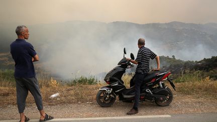 Deux hommes regardent l'incendie de forêt qui s'est déclaré, à proximité du village de Zberber, dans la province de Bouira (Algérie), le 24 juillet 2023. (APP / NURPHOTO)