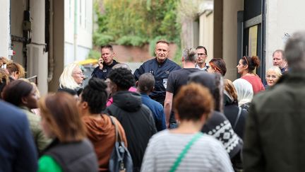 Des policiers français montant la garde tandis que des proches attendent devant l'entrée du lycée Gambetta à Arras, le 13 octobre 2023, où un enseignant a été tué lors d'une attaque au couteau. (FRANCOIS LO PRESTI / AFP)