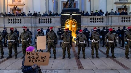 Une manifestante tient une pancarte "vous avez du sang sur les mains" près de militaires postés devant l'église de la Sainte-Croix, à Varsovie (Pologne), le 30 octobre 2020. (WOJTEK RADWANSKI / AFP)