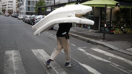 Un migrant porte son matelas sur la rue de Flandres à Paris après l'écvacuation par la police, le 6 septembre 2016 (MATTHIEU ALEXANDRE / AFP)