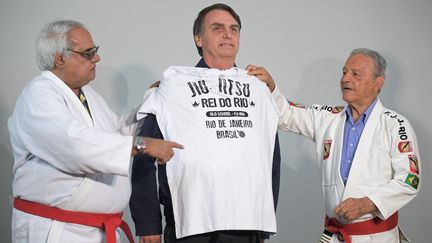 Jair Bolsonaro recevant un tee-shirt de Robson Gracie (droite), fils du fondateur de "Gracie Jiu-Jitsu".&nbsp; (CARL DE SOUZA / AFP)