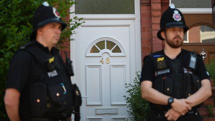 Deux policiers britanniques montent la garde devant la porte d'un domicile perquisitionné, le 26 mai 2017 à Manchester (Royaume-Uni), quatre jours après un attentat. (OLI SCARFF / AFP)