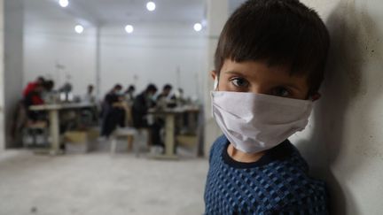 Un enfant syrien dans un atelier de couture où des volontaires fabriquent des masques pour lutter contre le coronavirus, à Idleb. (AAREF WATAD / AFP)