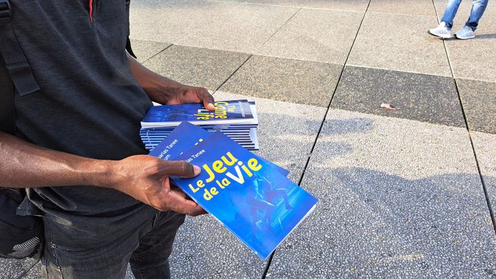 Un membre de la Communauté missionnaire chrétienne internationale distribue des livrets près de l'Arena Paris La Défense, le 1er août 2024. (RAPHAEL GODET / FRANCEINFO)