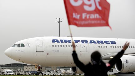 Une employ&eacute;e d'Air France agite un drapeau de la CGT devant un avion de la compagnie &agrave; l'a&eacute;roport de Roissy, le 1er octobre 2015. (KENZO TRIBOUILLARD / AFP)