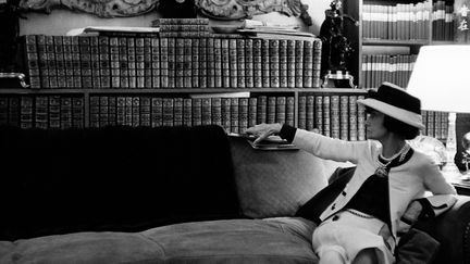 Portrait de Gabrielle Chanel sur son canapé, regardant sa bibliothèque Juillet 1962 - Photographie Collection Douglas Kirkland, Los Angeles
 (Douglas Kirkland)