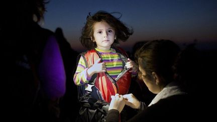 Kos, le 13 août 2015. Symbole de l'immigration qui arrive en Grèce, cette fillette, tout juste débarquée de son canot en provenance de Turquie, se fait enlever son gilet de sauvetage.  (ANGELOS TZORTZINIS / AFP)