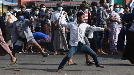 Des soutiens de la junte militaire lancent des projectiles à l'encontre d'habitants, le 25 février 2021 à Rangoun. (SAI AUNG MAIN / AFP)