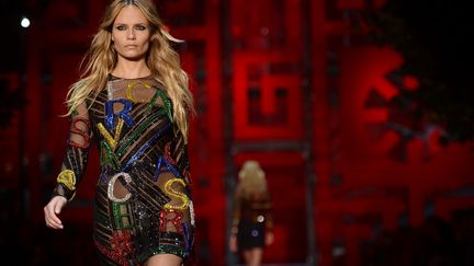 Versace s'inscrit en contre-tendance, prônant le retour à une mode-logo revendiquée et hyper sexy. Pas sûr que les cuissardes colorées en daim ou vernies dans des rouge, jaune et vert pétants soient des plus pratiques, mais quelle allure !  Les couleurs primaires, proposées en total look ou par flash en zébrures et bandes illuminant des robes noires, insufflent une énergie à une collection très pop. Les grosses lettres multicolores composant le nom de la griffe dansent la java sur des pulls, quand ce n'est pas tout simplement Versace bien visible en vert sur un sweat-shirt noir. Quant à la frise grecque, autre symbole maison, elle est déclinée un peu partout en micro-dessins ou en format géant sur des ensembles multicolores, ou plus discrète, décorant une paire de collants, les manches d'un manteau, le bord d'une veste ou encore une ceinture.
 (FILIPPO MONTEFORTE / AFP)