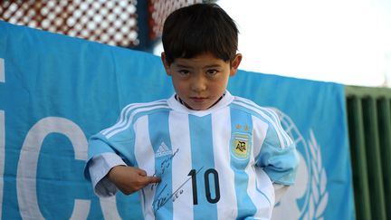 Murtaza, garçon afghan de 5 ans, fan de Lionel Messi, montre la signature de son idole sur le maillot argentin que le joueur lui a dédicacé, le 25 février 2016 à Kaboul (Afghanistan). (MAHDY MEHRAEEN / UNICEF AFGHANISTAN / AFP)