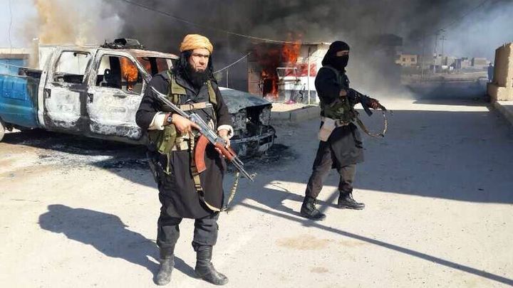 Une personne pr&eacute;sent&eacute;e comme un leader de l'Etat islamique en Irak et au Levant (G) se tient devant des voitures en feu, le 8 janvier 2014, dans un lieu ind&eacute;termin&eacute; en Irak. (HANEIN.INFO / AFP)