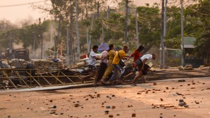 Des habitants courent près d'une barricade pendant des affrontements entre forces de l'ordre et manifestants à Hlaing Tharyar, près de Rangoun (Birmanie), le 14 mars 2021. (STR / AFP)