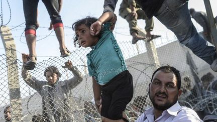 Une fillette syrienne extirpée entre grillages tordus et barbelés menaçants au point de passage d'Akçacale, entre la Syrie et la Turquie, le 14 juin 2014. La photo a reçu le Visa d'Or News au Festival international de photojournalisme «Visa pour l'image» de Perpignan, le 5 septembre 2015. (Bulent Kiliç/AFP)