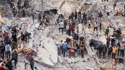 Des civils et des sauveteurs cherchent des survivants parmi les décombres d'un bâtiment détruit à la suite d'un bombardement israélien à Khan Younes, dans le sud de la bande de Gaza, le 12 novembre 2023. (MAHMUD HAMS / AFP)