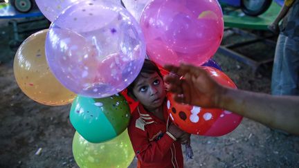 Un petit gar&ccedil;on &acirc;g&eacute; de cinq ans aide son p&egrave;re vendeur de ballons &agrave; Bombay (Inde), le 8 d&eacute;cembre 2014. (DANISH SIDDIQUI / REUTERS)