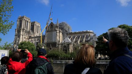 Des passants prennent en photo la cathédrale Notre-Dame de Paris et des ouvriers au travail, le 29 avril 2019, deux semaines après l'incendie qui a détruit la voute et la flèche de l'édifice. (GONZALO FUENTES / REUTERS)