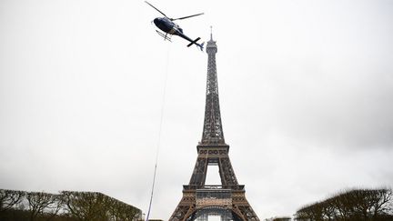 Un hélicoptère part de la Tour Eiffel, à Paris, après avoir hélitreuillé une nouvelle antenne de 6 mètres de hauteur au sommet de la Tour Eiffel le 15 mars 2022. (CHRISTOPHE ARCHAMBAULT / AFP)