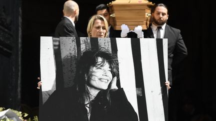 Le cercueil de Jane Birkin sort de l'église Saint-Roch à Paris, le 24 juillet 2023, devancé par un portrait de la chanteuse et actrice, morte le 16 juillet à l'âge de 76 ans. Outre son talent d'artiste, l'icône franco-britannique laisse derrière elle l'image d'une femme engagée, défendant notamment le droit à l'avortement et l'accueil des sans-papiers. (JULIEN DE ROSA / AFP)