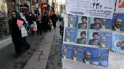 Des Iraniens passent devant des affiches électorales, le 24 février 2016, à Qom (Iran). (ATTA KENARE / AFP)