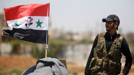 Un soldat de l'armée syrienne à côté d'un drapeau syrien portant l'effigie de Bachar Al-Assad, le 10 juillet 2018, à Deraa en Syrie. (Photo d'illustration) (OMAR SANADIKI / REUTERS)