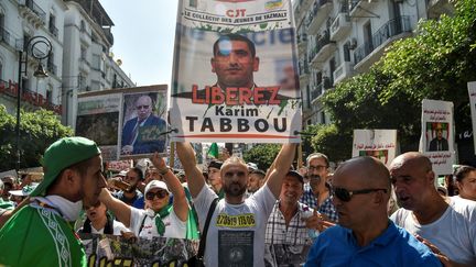 Portrait de Karim Tabbou brandi par les manifestants lors d'un rassemblement dans les rues d'Alger, le 27 septembre 2019, au lendemain de son arrestation. Karim Tabbou est devenu l'un des principaux visages du Hirak, le mouvement de contestation algérien. (RYAD KRAMDI / AFP)