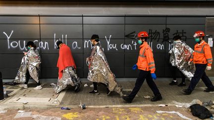 Des protestataires&nbsp;emmenés par des soignants vers des ambulances, sur le campus polytechnique de Hong Kong. (ANTHONY WALLACE / AFP)