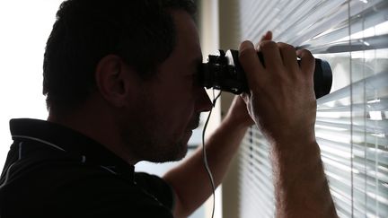 Un homme surveille à travers des stores. (MAXPPP)