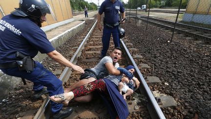 Les policiers hongrois tentent de d&eacute;gager une&nbsp;famille des migrants des rails, &agrave; la gare de&nbsp;Bicske (Hongrie), le 3 septembre 2015. (LASZLO BALOGH / REUTERS )