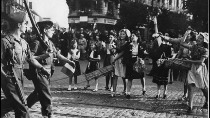 Des jeunes filles et des enfants jettent des fleurs aux soldats de la 1ere Armee française qui viennent de libérer la ville de Dijon. Photographie 11 septembre 1944. (LEEMAGE VIA AFP)